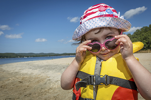 A little girl looking over her heart-shaped sunglasses while wearing a life jacket