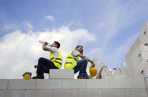 Two construction workers sitting on a wall, one drinking water