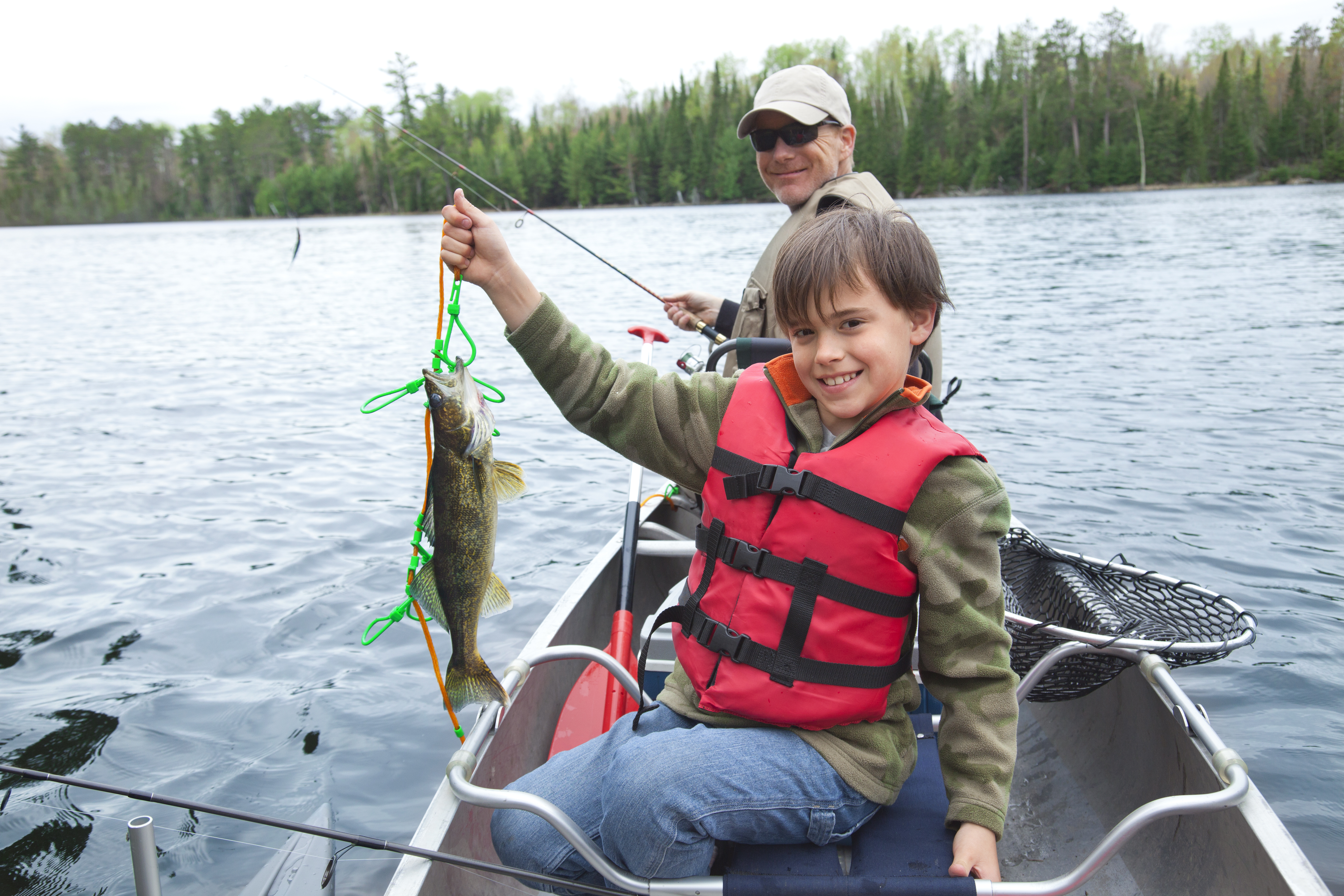 Boy smiling and wearing a life jacket while holding up a fish