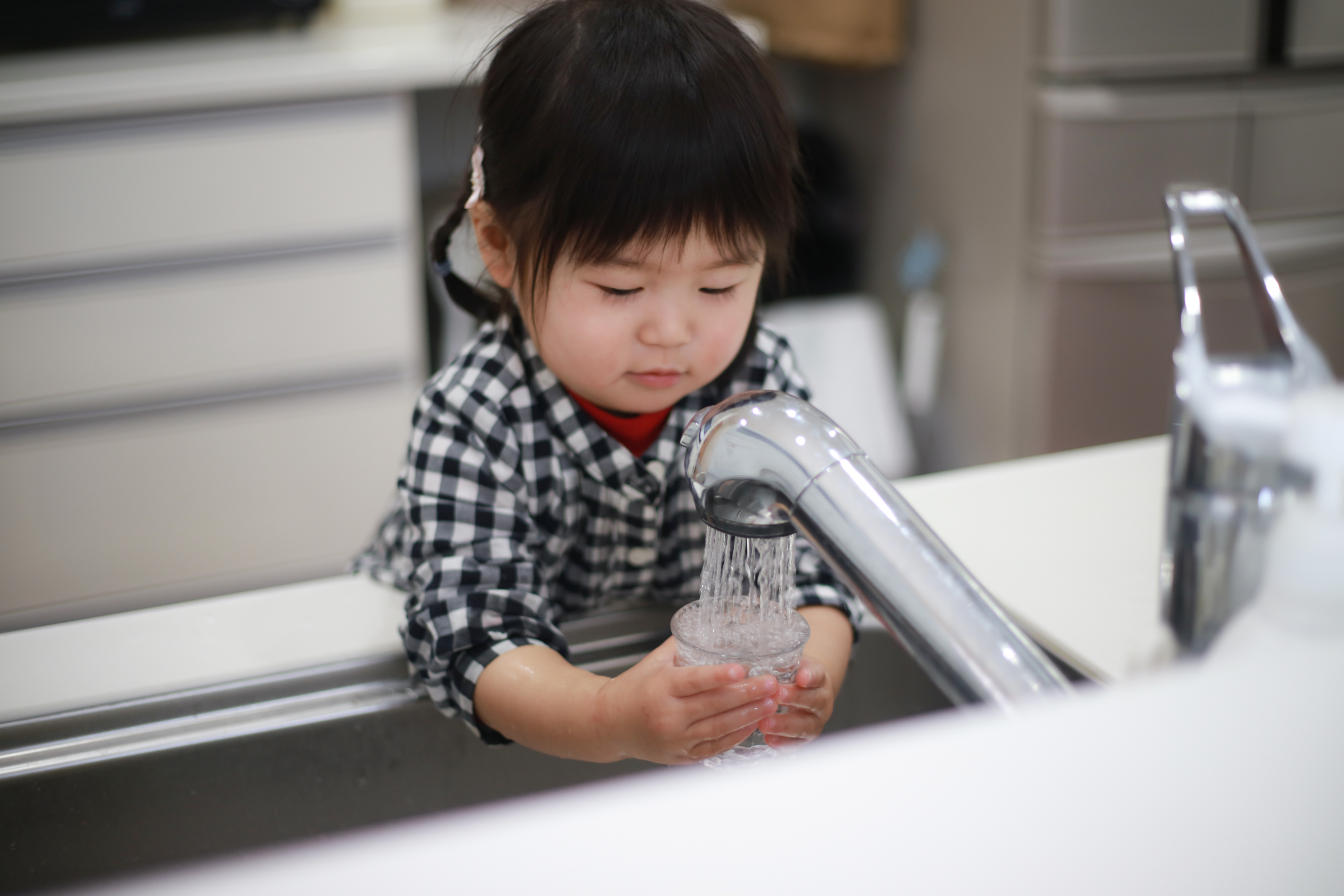 Little girl getting a glass of water from the faucet