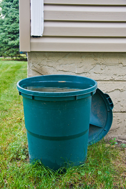 Large trashcan with the top off sitting under a rain gutter in order to catch rainwater
