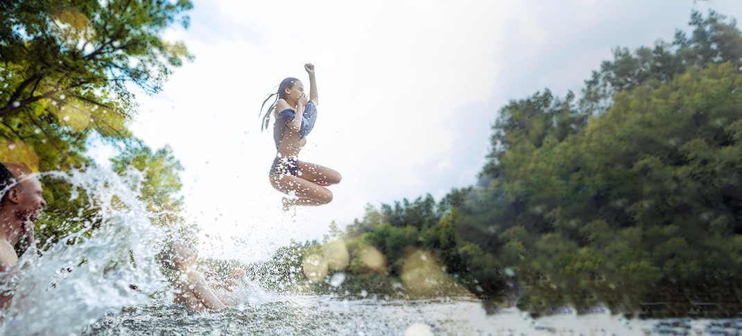 A girl jumping into the water while holding her nose