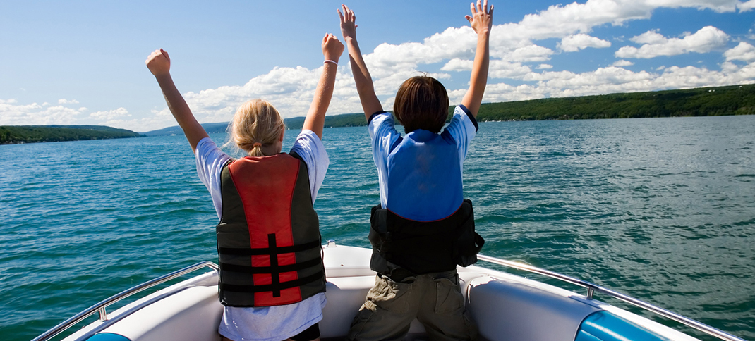 Two kids in a boat wearing life jackets with their hands in the air