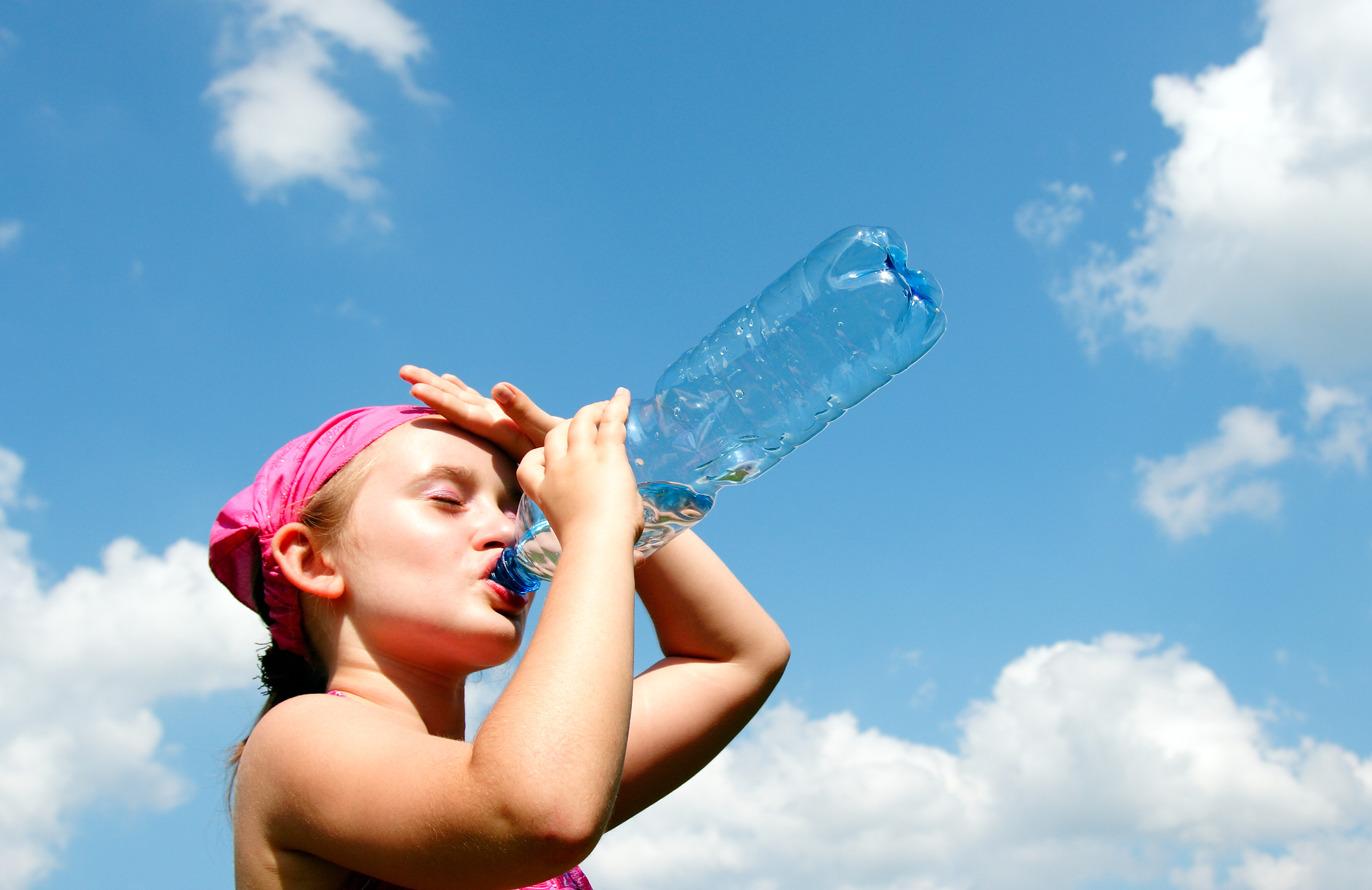 A child drinking water in front of a blue sky with white clouds